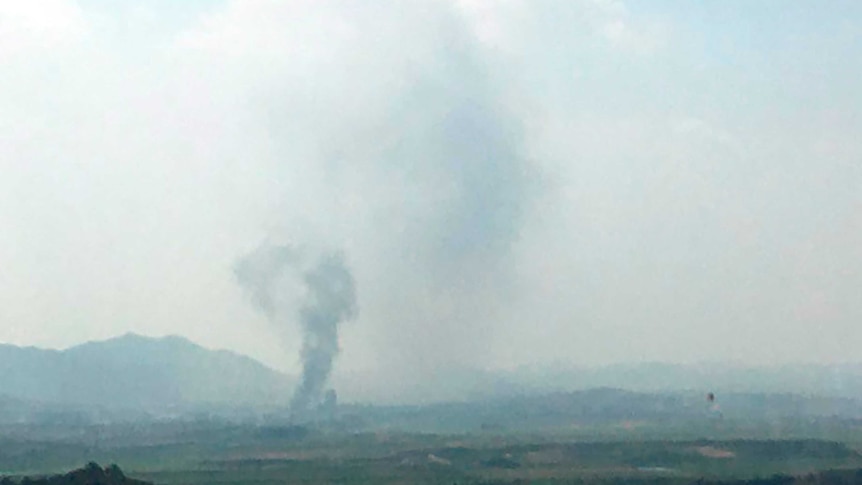 Smoke is seen rising from a distant valley into a cloudy sky.