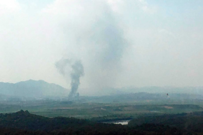 Smoke is seen rising from a distant valley into a cloudy sky.