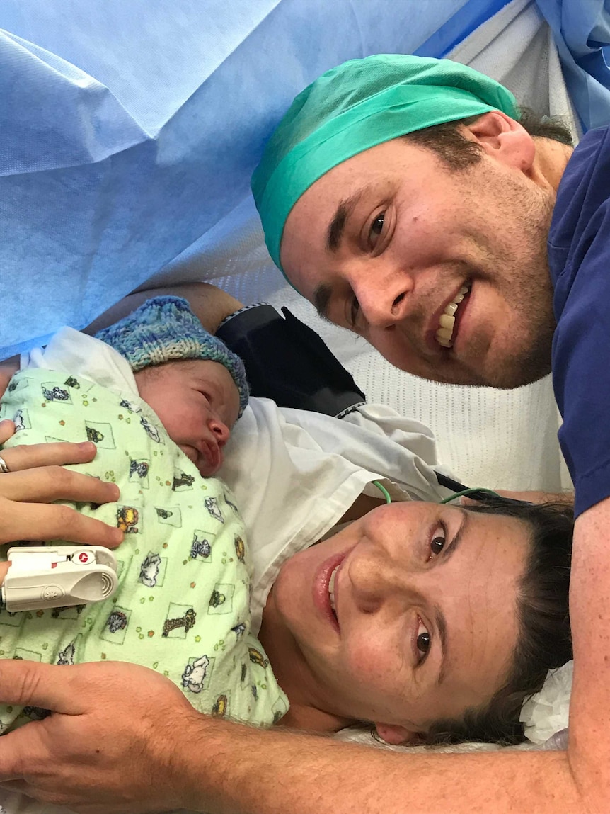 A woman and man smile as they hold their newborn baby after a shared GP pregnancy.