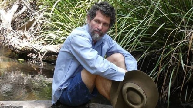 Peter Ridd sitting on a log above a bush creek
