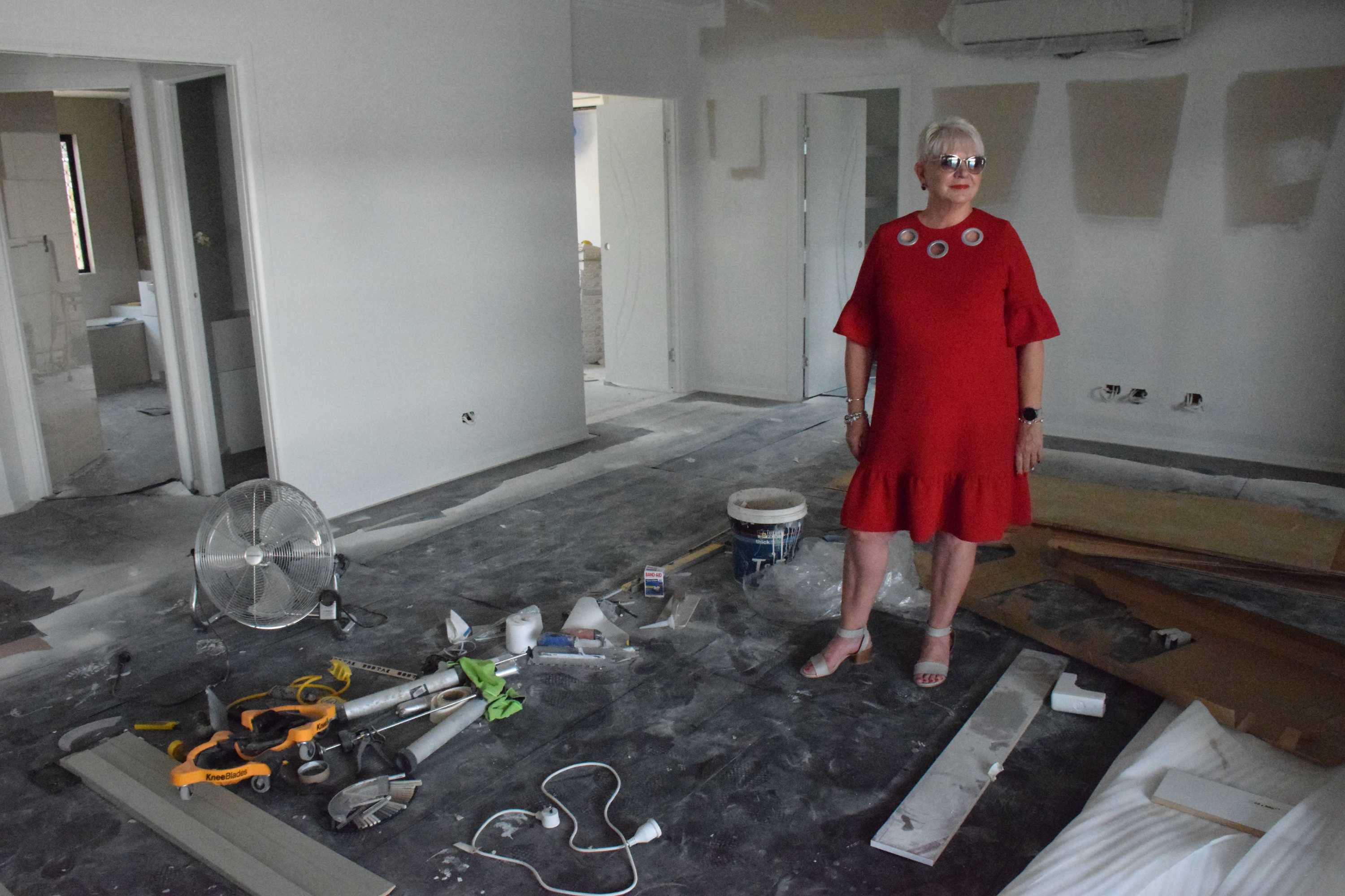 Woman in bright red dress stands in her demolished house and looks out to the pool