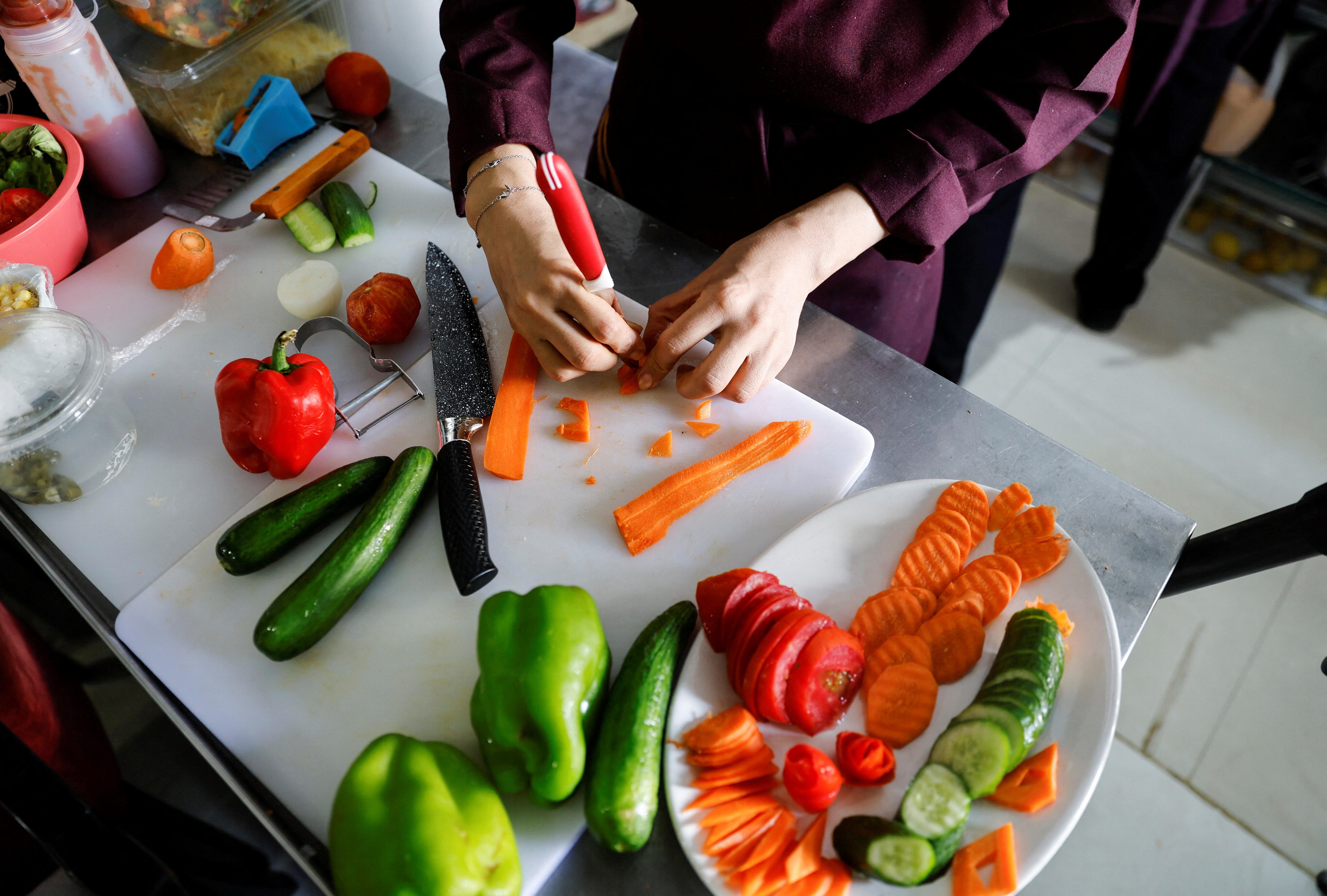 Birds eye view of a person cutting carrots, capsicum, cucumber and tomato