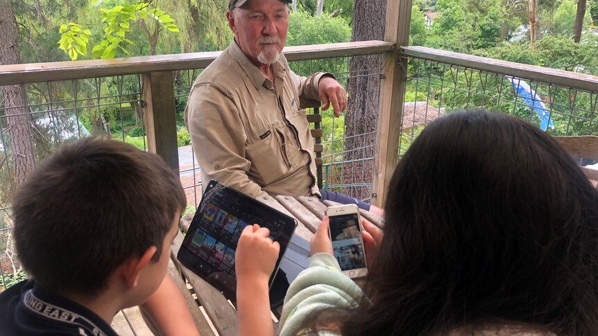 A man sits at a table with his kids who are using ipads