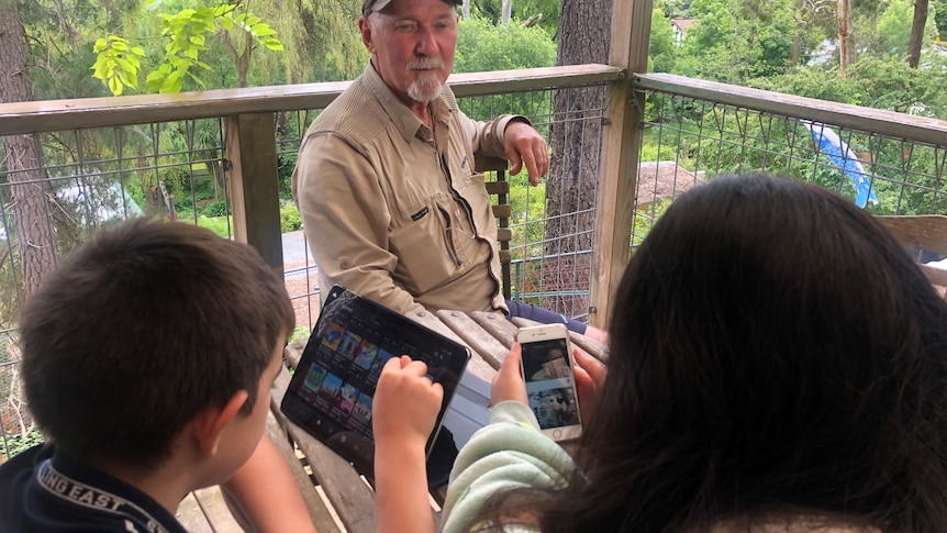 A man sits at a table with his kids who are using ipads