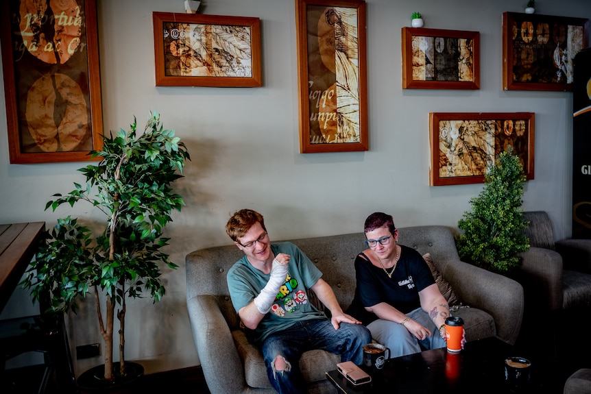 A young man and a woman sitting on the couch drinking coffee.