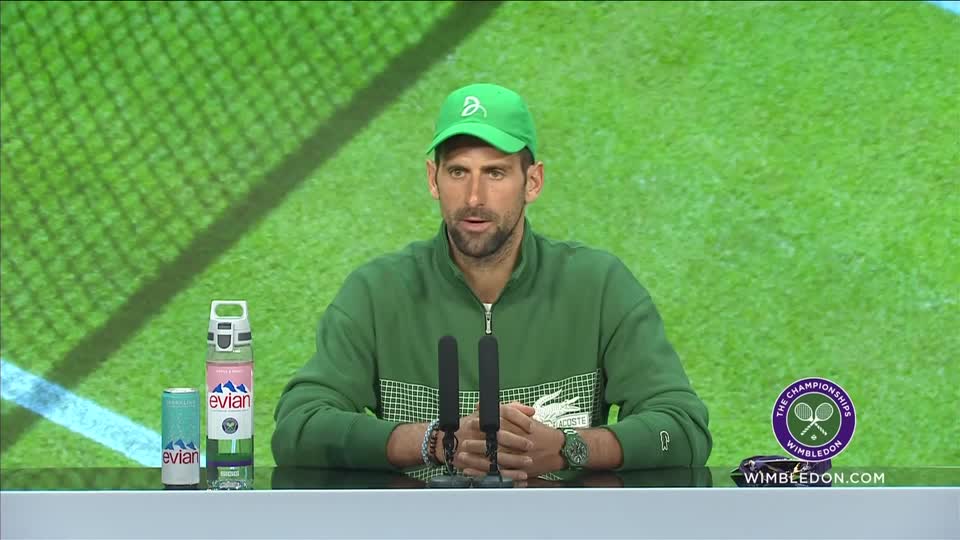 Novak Djokovic wearing forest green sweatshirt, baseball cap and watch against green tennis court background