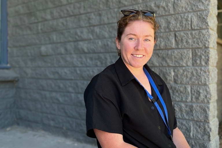 woman in dark top smiles at camera sitting on entrance steps in the shade with sunglasses on her head 