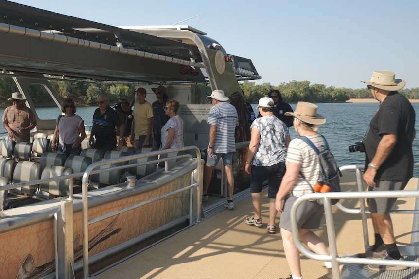 Tourists with hats and backpacks board a boat.