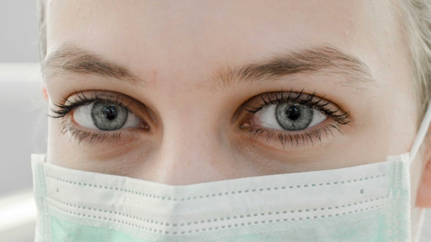 A woman wearing a mask looking at the camera.