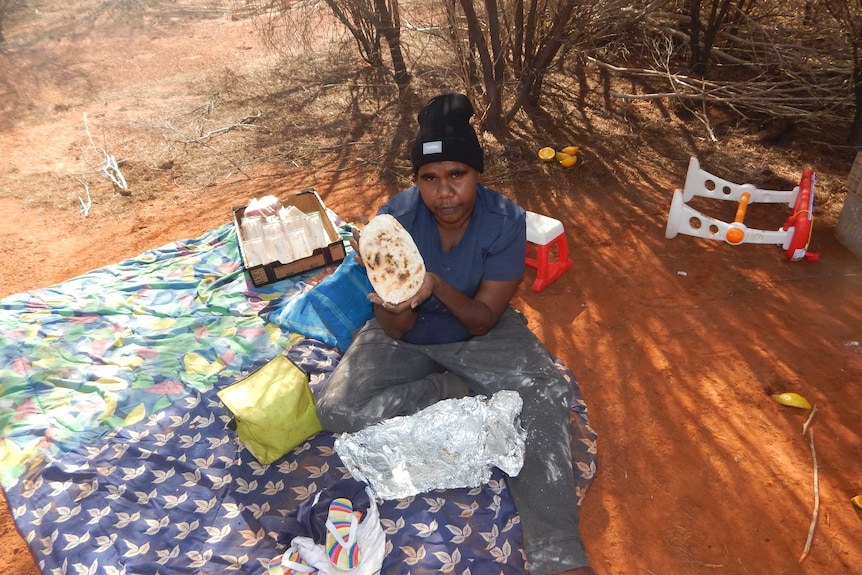 Verna Wilson sits on a picnic blanket and holds up some damper she made for her family.