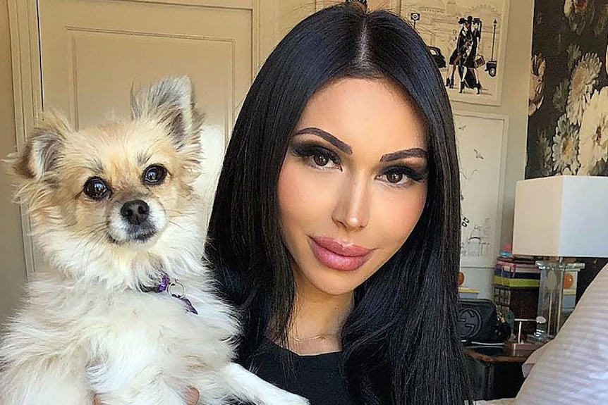 A woman holds a small dog towards the camera.