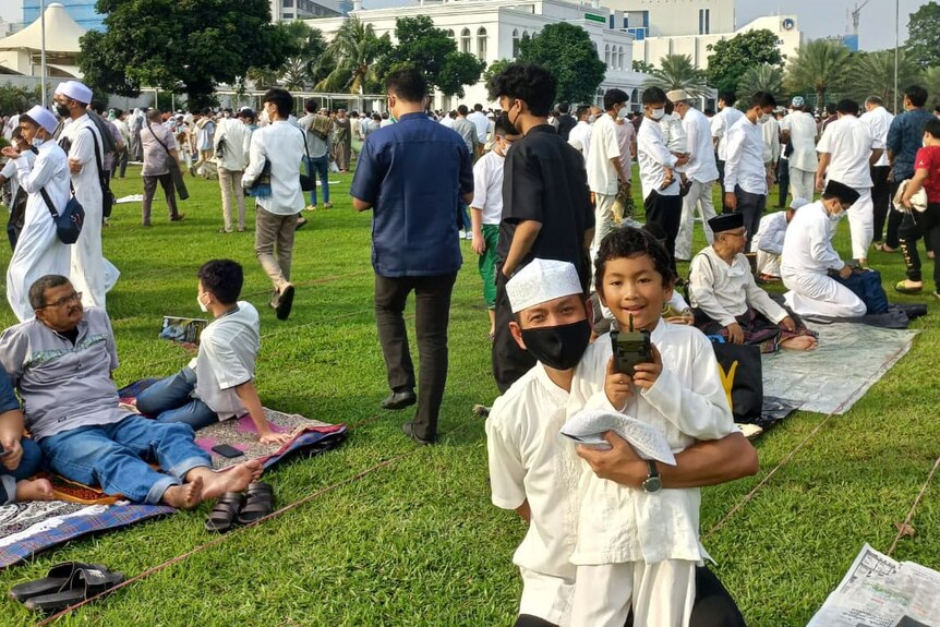 A man and a boy wearing masks in front of other prayers in a field.