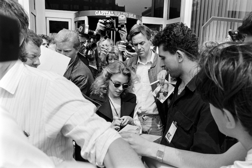 A black-and-white photo of Kylie Minogue signing autographs in 1989.