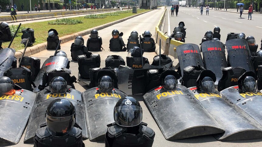 Black Indonesian riot gear is discarded on the road in Jakarta, arranged in straight lines.