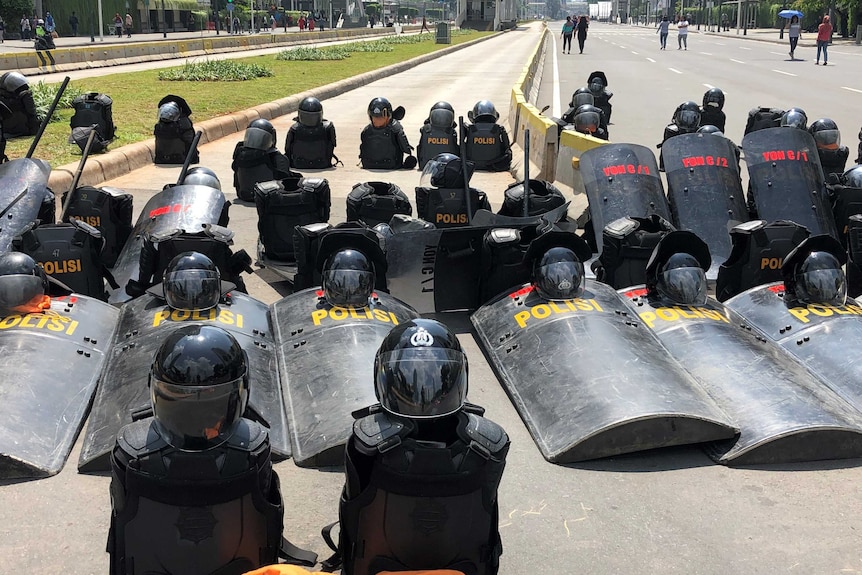 Black Indonesian riot gear is discarded on the road in Jakarta, arranged in straight lines.