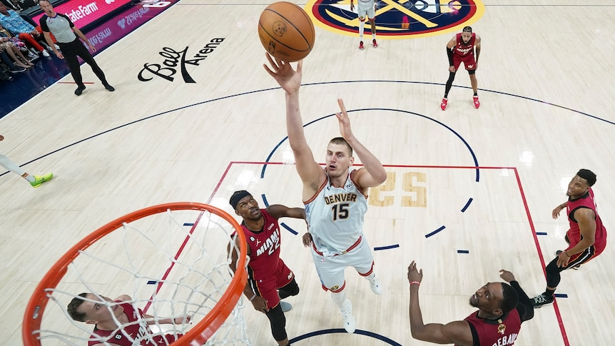 A tall NBA basketballer raises his arm up to shoot the ball toward the basket as he is surrounded by opposition players.