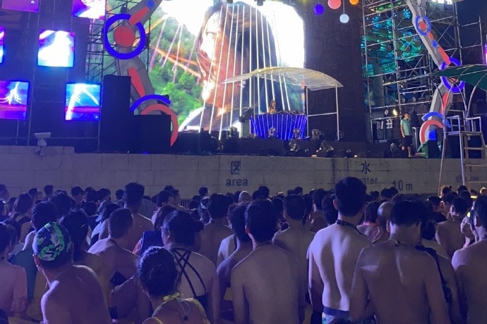 Attendees of a music festival at a water park in Wuhan, China. There is a large stage and a big crowd of people.