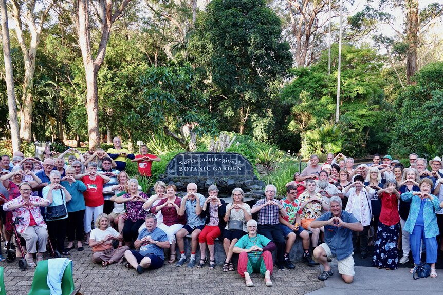 Dozens of people make heart shapes with their hands in front of North Coast Regional Botanic Gardens