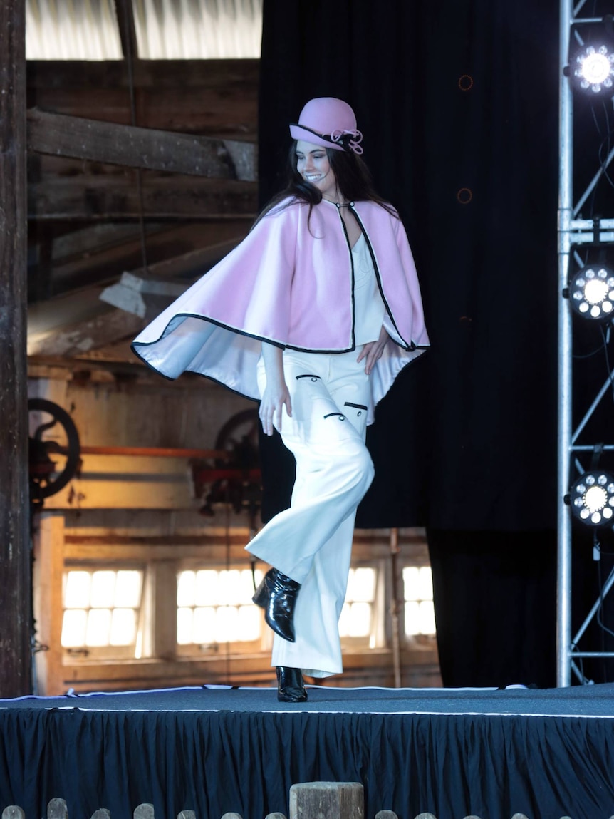 A woman in a pink and white outfit walks on a runway.