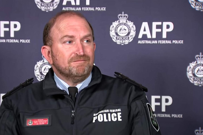 A uniformed male police officer sits in front of AFP signage.