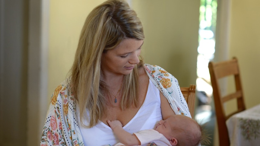 Woman looks down ay her sleeping newborn baby.