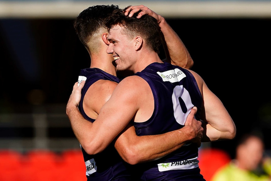 Two Fremantle players smile as they hug each other