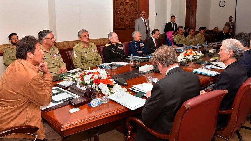 Imran Khan sits at the head of a mahogany table surrounded by military generals and government leaders.