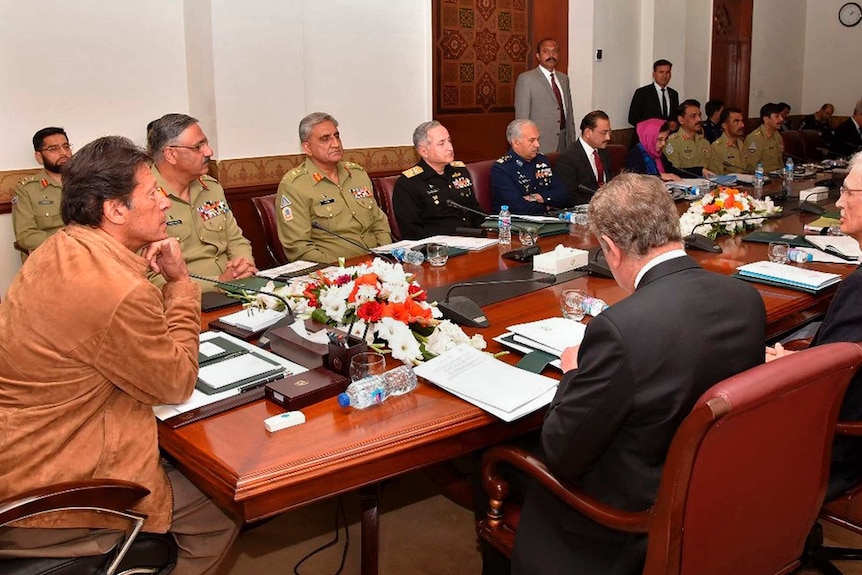 Imran Khan sits at the head of a mahogany table surrounded by military generals and government leaders.