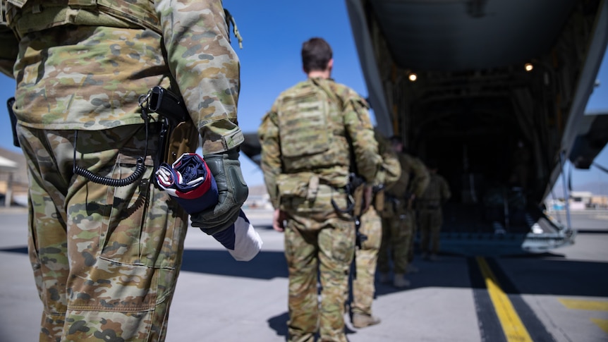 A soldier holds a rolled up Australian flag as he prepares to board a military aircraft.