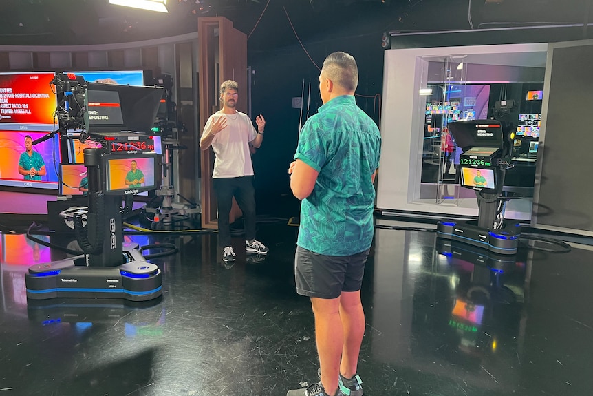 Two men talking in a TV studio standing next to cameras.