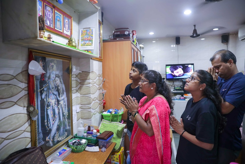 A man, a woman in a pink sari, a teen girl and a teen boy pray to an Indian shrine