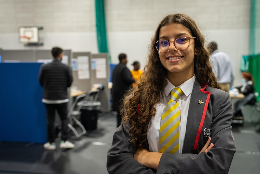 A schoolgirl smiles and poses for the camera inside a gym.