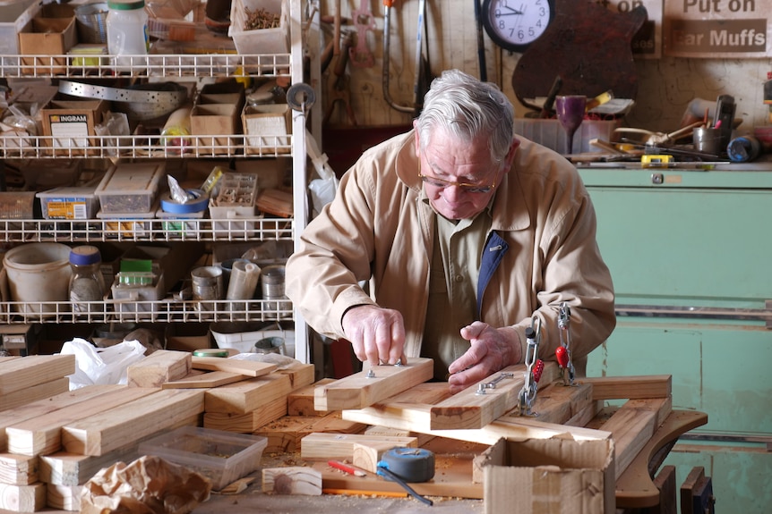 An elderly man building a wooden chair 