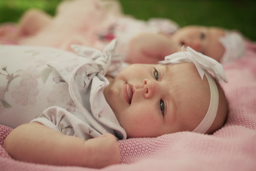 Twin girls lay on a pink blanket.