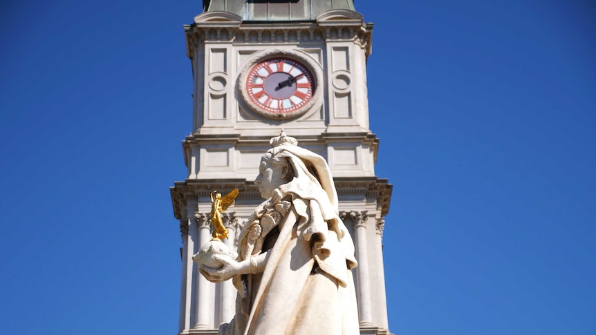 A statue in front of a clock tower.