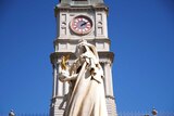 A statue in front of a clock tower.
