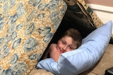 11-year-old Ezekiel Coutts smiles for a photo from within his home-made fort assembled with mattresses and cushions.
