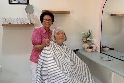 A woman with an elderly lady sitting on a hairdressers chair
