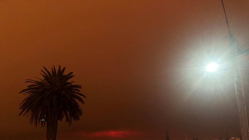 The sky is black and orange and there are cars parked.