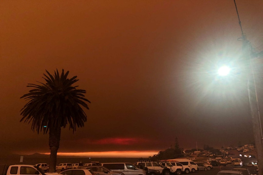 The sky is black and orange and there are cars parked.