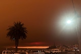 The sky is black and orange and there are cars parked.