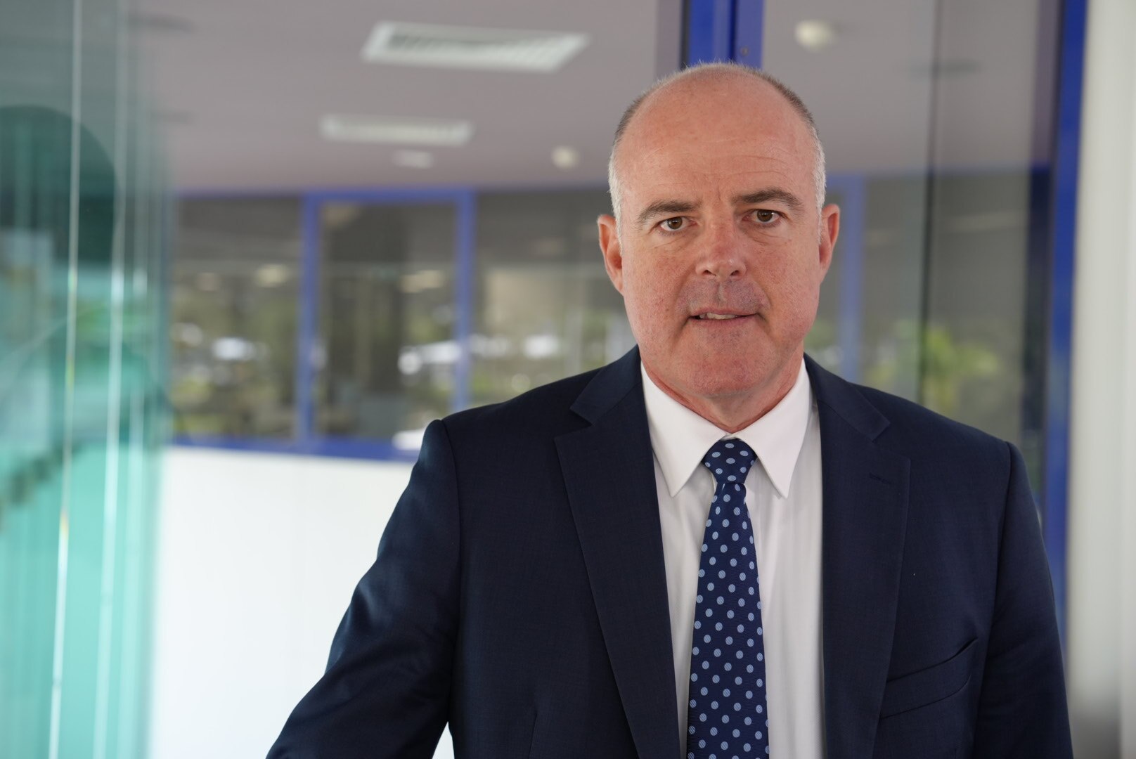 A man in a suit smiles for a portrait in an office building.