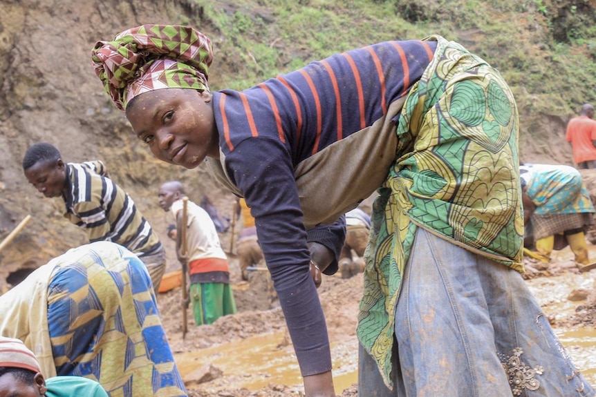 A woman in colourful clothes bends over and picks up stones.