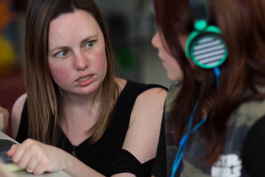 Crouched down to her level, teacher Anita Harding explains something to a student.