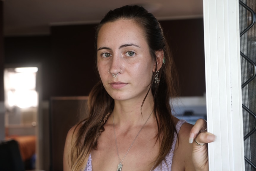 a woman stands in her door looking with a serious expression at the camera