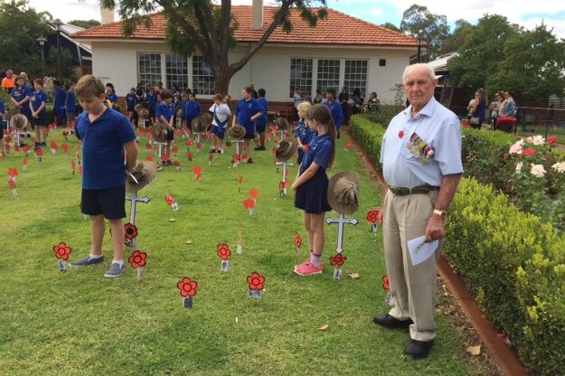 Len Snell stands on a lawn with school children with their paper poppies stuck in the lawn.