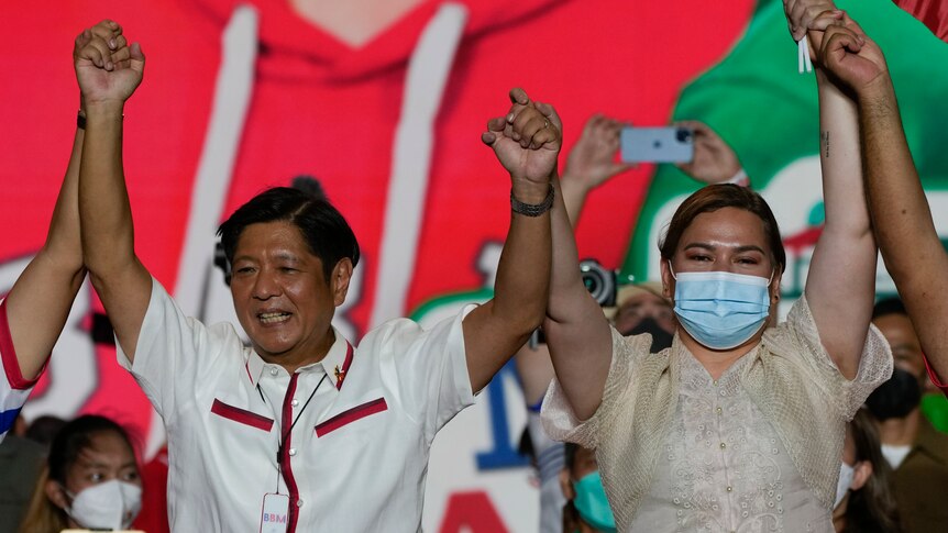Ferdinand 'Bongbong' Marcos Jr and Sara Duterte, wearing a mask, raise their hands in celebration on stage