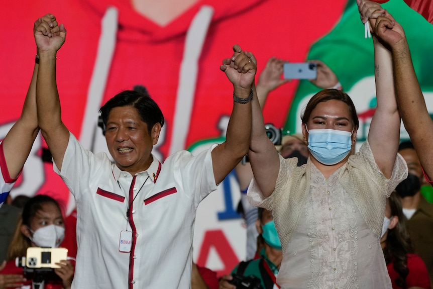 Ferdinand 'Bongbong' Marcos Jr and Sara Duterte, wearing a mask, raise their hands in celebration on stage