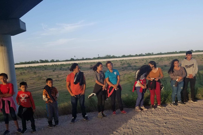 Women, men and children line up on the side of a dirt road