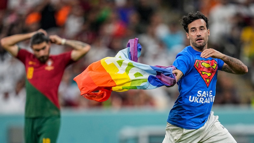 A man in a blue superman shirt flying a rainbow flag